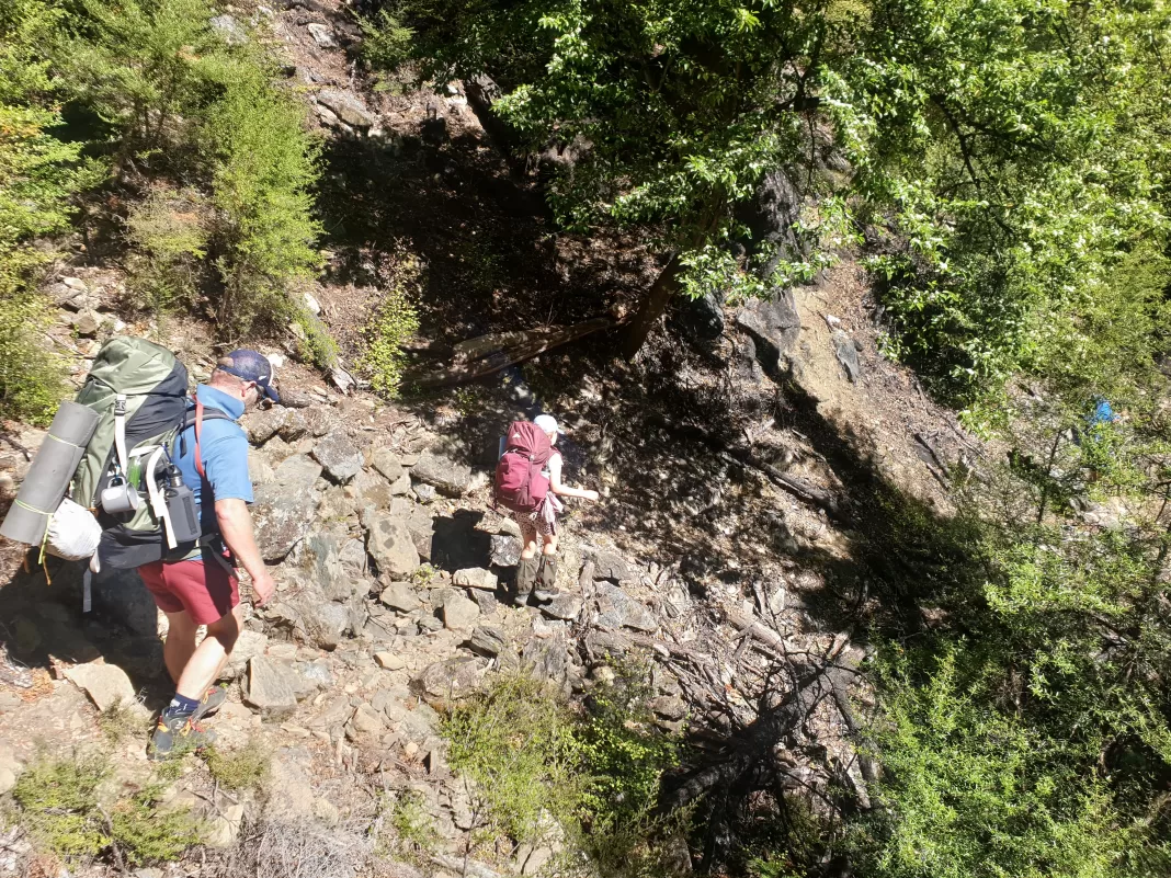 Man and a child with full tramping back traversing a rocky slope