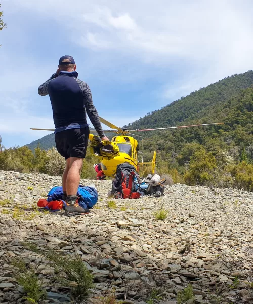 Tramping rescue story - man walking towards yellow helicopter landed on scree field