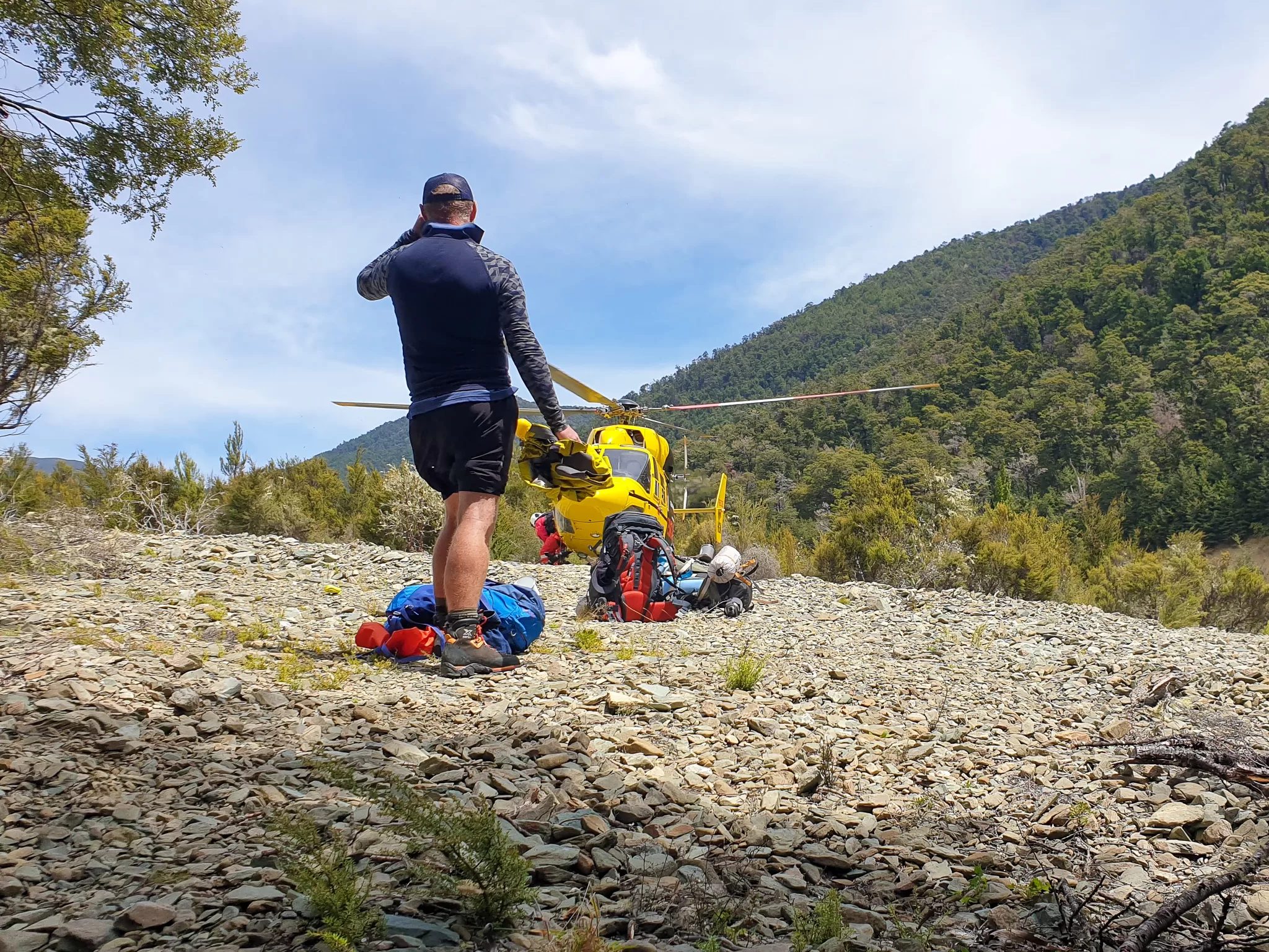 Tramping rescue story - man walking towards yellow helicopter landed on scree field