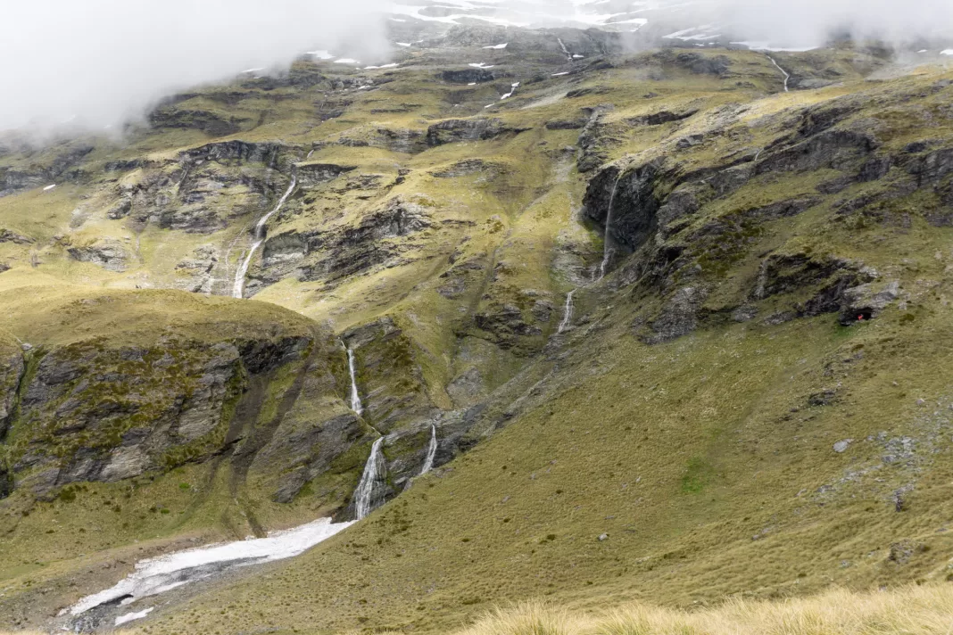 Photo of the upper rock bivy above Kea Basin on the way to Mt Earnslaw, with waterfalls flowing over snowy bluffs