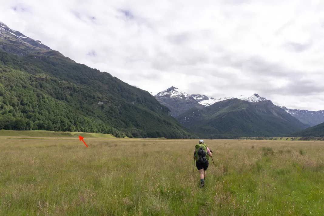 Tramper walking up the Rees Valley with a red arrow pointing towards where the Kea Basin Track starts