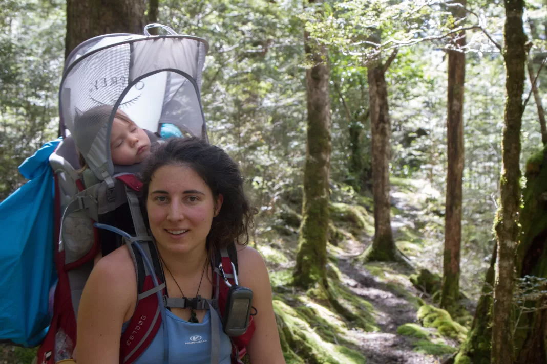 Woman tramping in the New Zealand bush with a baby asleep in the backpack carrier