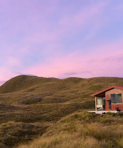 Mataketake Hut at sunrise with two people outside on the deck
