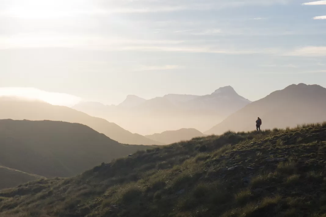 Tramper standing silhouetted by sunrise in front of mountain peaks