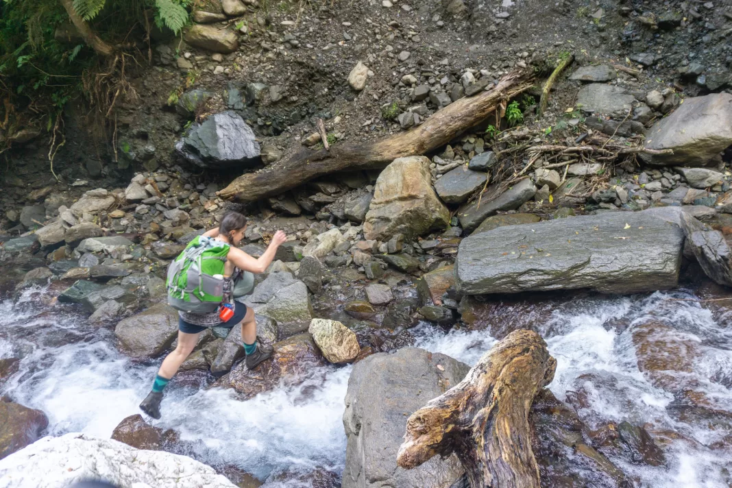 Tramper jumping across a stream on the Haast to Paringa Cattle Track