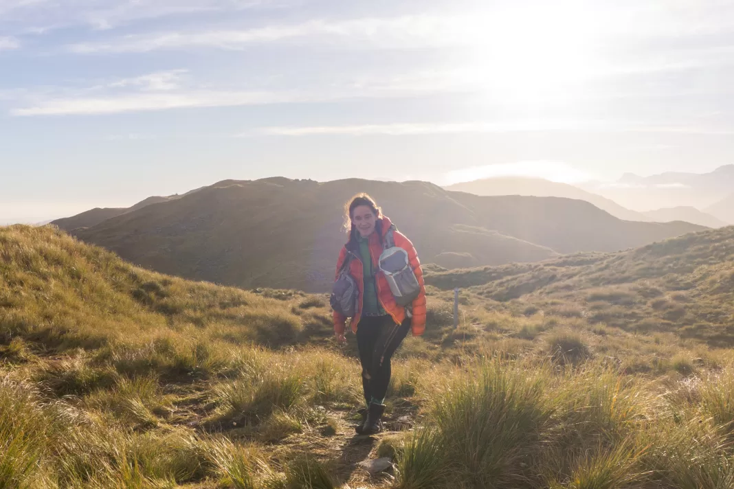 Woman wearing an Aarn pack tramping at sunrise in the mountains