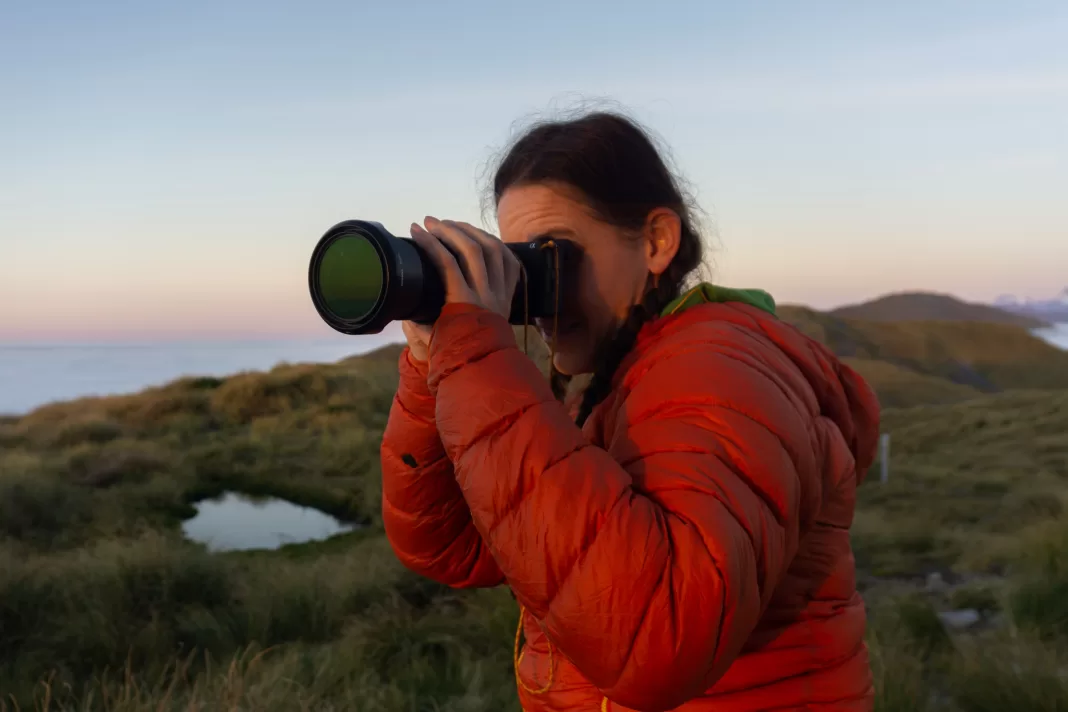 Woman holding a large camera at sunset in the mountains
