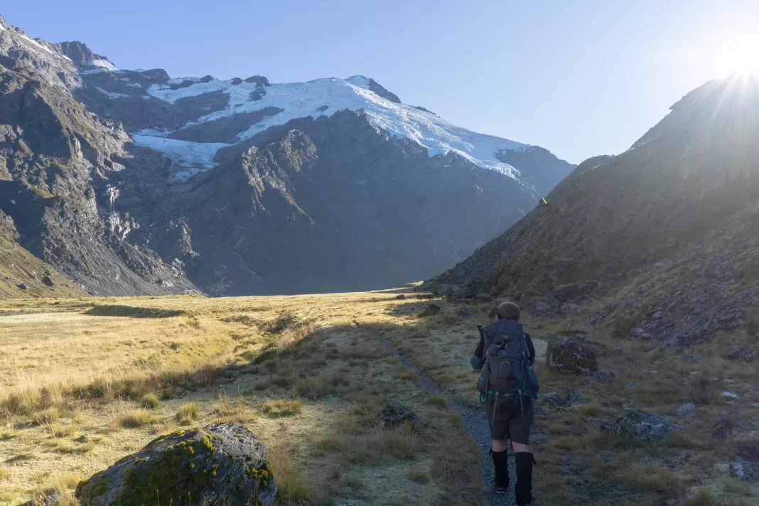 Woman walking along a track with Mt Edward and the Marshall and Hesse Glaciers in the background