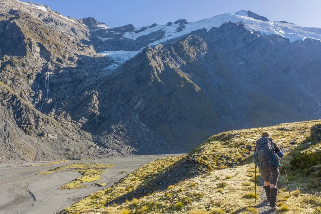 Woman walking up the Dart Valley with hanging glaciers and snowcapped mountains in the background