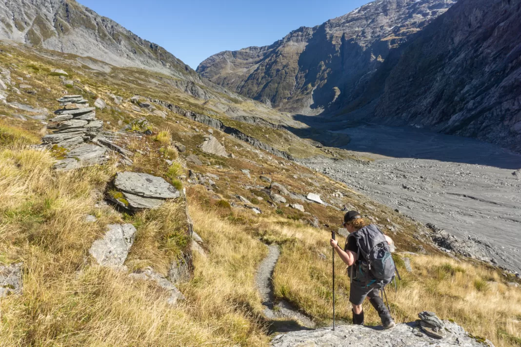 Woman walking along a track in tussocks with mountains in the background