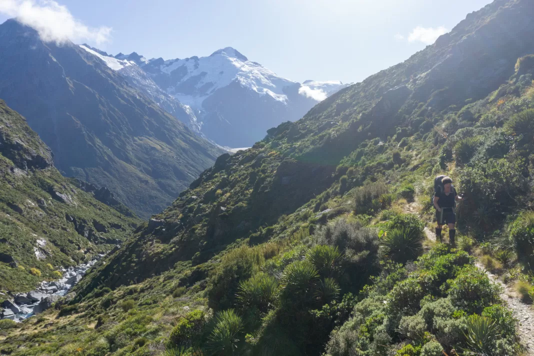 Tramper walking along the Rees Dart Track with mountains and glaciers in the background