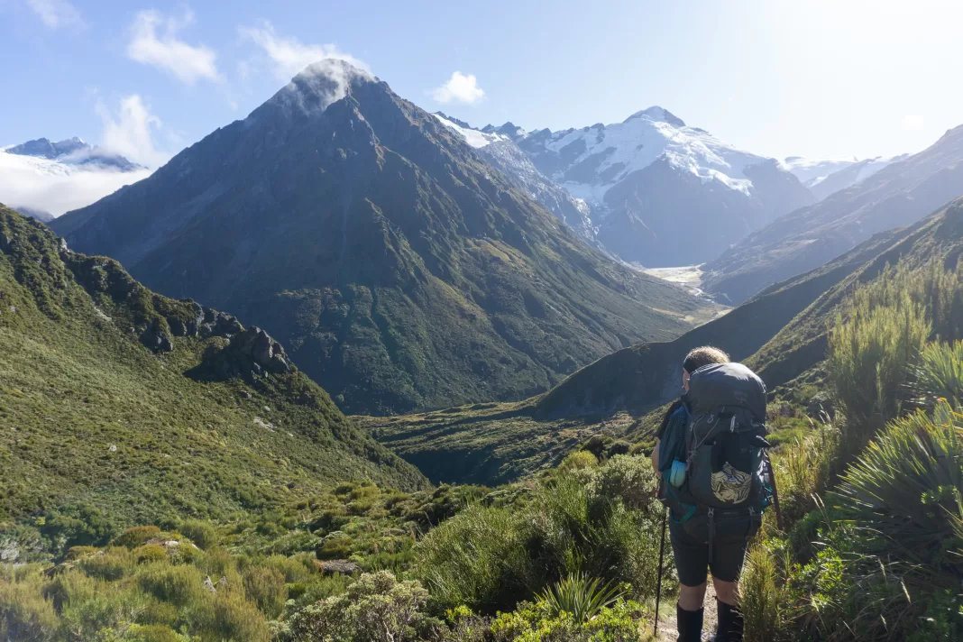 Tramper standing on the Rees Dart Track with a beautiful view of mountains and glaciers in front of them