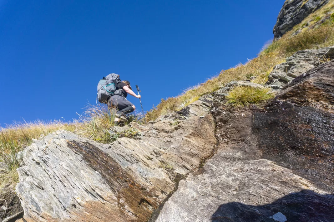 Woman climbing up steep terrain on the Rees Dart Track