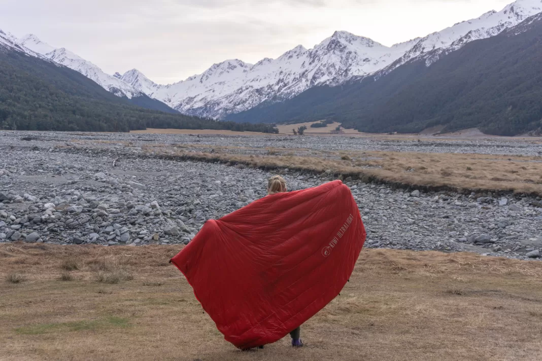 Tramper holding a Kiwi Ultralight quilt in front of snowy mountains
