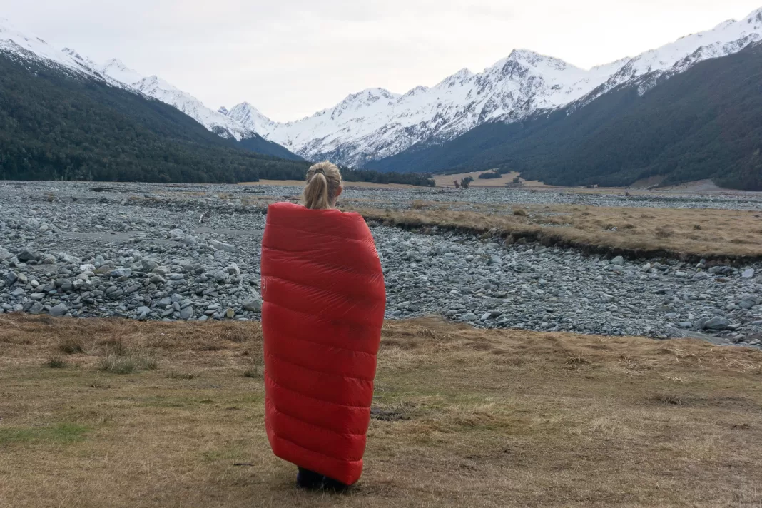 Tramper standing in front of mountains cosied up in a tramping quilt