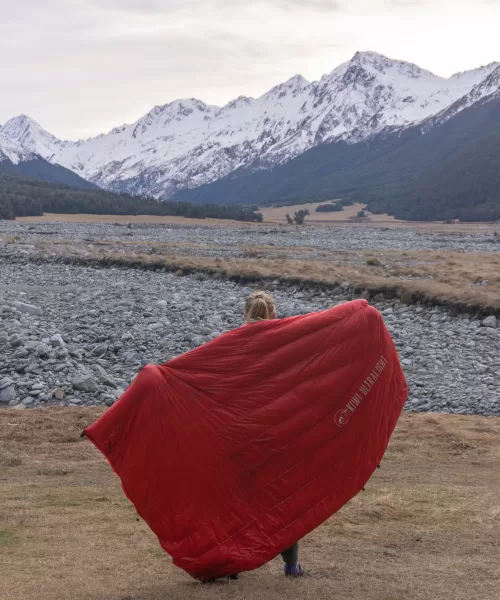 Tramper holding a Kiwi Ultralight quilt in front of snowy mountains