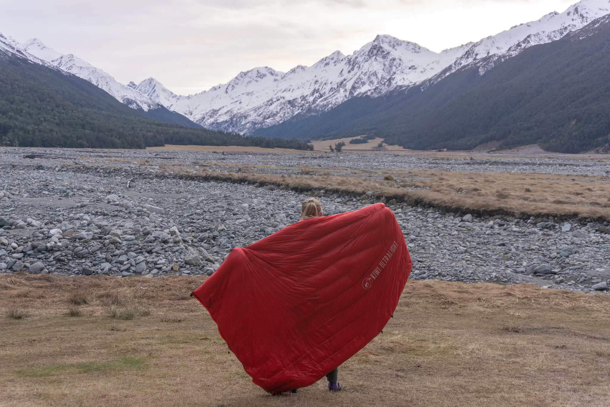 Tramper holding a Kiwi Ultralight quilt in front of snowy mountains