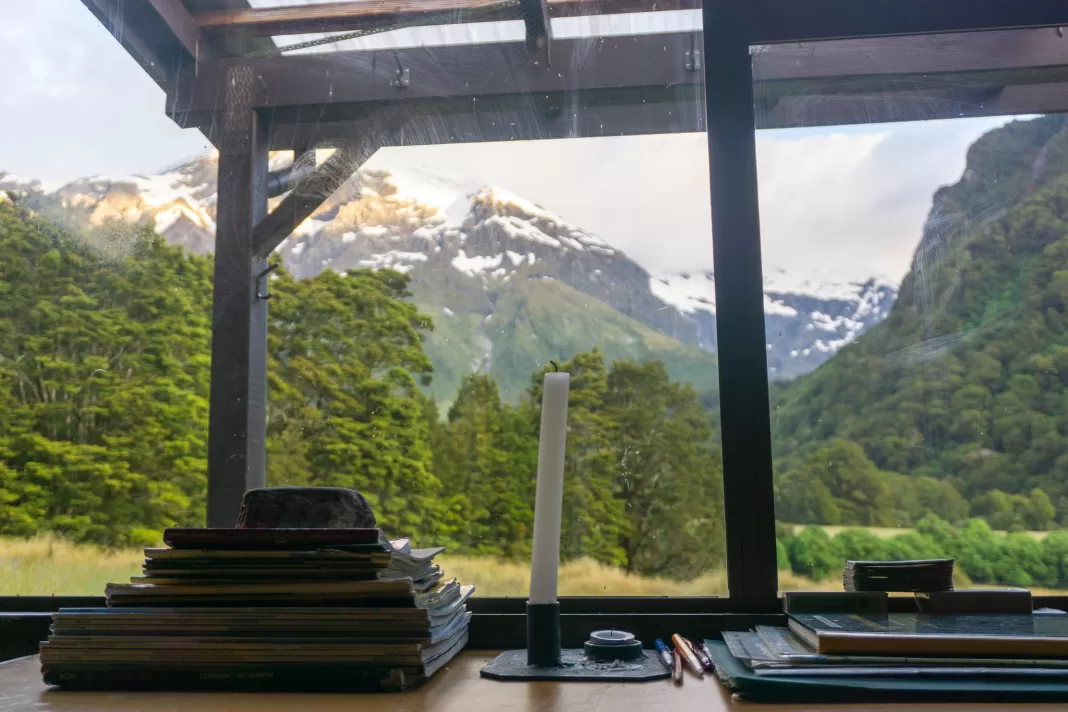 Photo from Top Forks Hut showing a candle, magazines, the DOC Intentions book and the mountain view outside